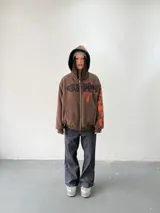 Campera reversible con cierre frontal. Un lado confeccionado en algodón color marrón con estampa plastisol en color naranja, bordados con apliques y capucha. El otro lado confeccionado en tela polar de pelo largo color negro con capucha.