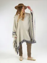 Poncho de hilo color crudo, con diseño de rayas azules y flecos en los bordes. Cuenta con un escudo bordado en la parte posterior.