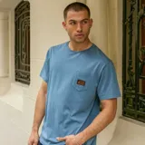 Remera azul de corte recto, manga corta y cuello redondo. Tiene un bolsillo en el pecho con etiqueta de la marca Volcom.