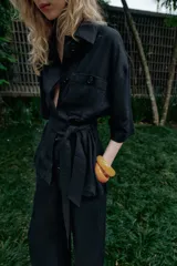 Chaqueta de estilo safari confeccionada en mezcla de lino, color azul marino, con cuello solapa, mangas cortas y cierre frontal con botones ocultos. Presenta bolsillos de parche en el pecho con solapa y botones, además de un cinturón ajustable del mismo tejido para anudar en la cintura.