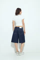 Bermuda de denim en color azul oscuro con diseño de rayas verticales blancas. Presenta un corte holgado, tiro medio y cierre frontal con botón y cremallera.