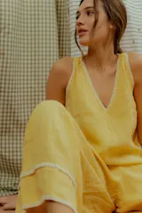 Mono largo de lino color amarillo, con escote en V, tirantes finos y detalles de costuras decorativas blancas en el escote y en los bajos de las piernas anchas.