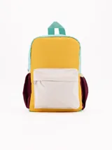Mochila pequeña de colores, con diseño colorblock en tonos menta, amarillo mostaza, blanco crema y bordó. Presenta un bolsillo frontal con tapa y cierre principal.