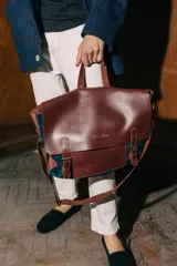 Maletín postman de cuero marrón y gamuza azul, con solapa frontal con hebillas, asa superior y correa ajustable para hombro.