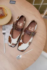 Ballerinas con estampado animal print de vaca, con correa de cuero marrón y hebilla dorada.