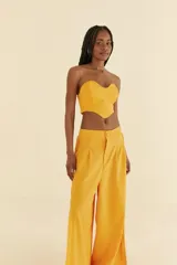 Pantalón amarillo de lino y viscosa, de pierna ancha, con cintura alta, pretina recta en la parte delantera y elástica en la parte trasera. Presenta detalle de trenza vertical en los laterales y aberturas en el dobladillo.