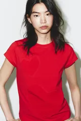 Camiseta roja de manga corta y cuello redondo, con un diseño de corazones en relieve o pespunte a tono en el frente.