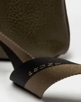 Bandolera color beige con correa ancha de tela negra con el nombre de la marca en blanco.