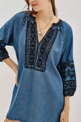 Vestido corto de tela tipo denim con bordados geométricos en color negro en el pecho y las mangas. Presenta escote en V, mangas tres cuartos con puños elásticos y un corte holgado.