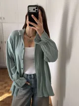 Sobrecamisa oversize de muselina verde pastel, de manga larga con puños fruncidos y cierre frontal de botones.