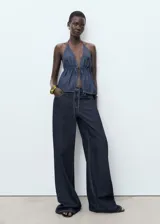 Top de denim con escote halter, espalda abierta y diseño evasé. Cuenta con fruncido elástico y cierre de lazo en el escote delantero.