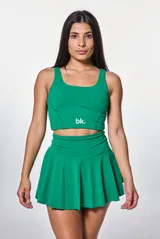Conjunto deportivo compuesto por un top de escote redondo con logo estampado y una pollera short con cintura alta y diseño plisado, ambos en color verde.