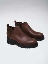 Botinetas negras con suela track, combinando cuero texturizado en la parte frontal y cuero charolado en la parte trasera. Diseño de caña baja con detalle de corte lateral.