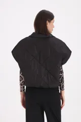 Chaleco acolchado negro con diseño de rombos, cierre frontal con cremallera y bolsillos laterales.