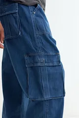 Pantalón tipo jean de corte baggy con diseño cargo, presenta bolsillos laterales amplios con solapa y costuras reforzadas. Confeccionado en denim de algodón con acabado lavado.