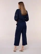 Pantalón crop de lino y algodón color blanco, con calce holgado, pierna ancha de corte recto y cintura elástica. Presenta bolsillos laterales y detalle de puntilla aplicada en el frente.