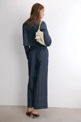 Pantalón de tiro medio confeccionado en denim azul oscuro, con diseño de pierna ancha, pinzas frontales y pespuntes a contraste. Cuenta con cierre frontal de cremallera y botón.
