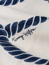 Chomba blanca de piqué de algodón con estampado de cuerdas azules. Tiene cuello polo, tapeta con botones y logo bordado en el pecho.