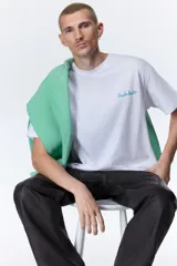 Remera blanca de corte holgado, con cuello redondo y diseño de manga corta. Cuenta con un pequeño estampado tipográfico en color verde en el pecho.