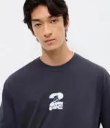 Remera de corte relajado color gris oscuro, con cuello redondo y manga corta. Presenta una estampa frontal pequeña en color blanco con el logo de Tupac.