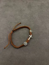 Set de tres pulseras ajustables de cordón con detalles religiosos. Incluye una pulsera roja con cruces, una pulsera marrón trenzada con cruz y medallas, y una pulsera verde con medalla colgante.