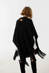 Ruana negra de tejido de punto con flecos y aplique de cuero vacuno con manchas blancas.