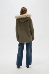 Campera parka de color verde militar, con cierre frontal oculto, bolsillos laterales con solapa y capucha fija con borde de piel sintética.