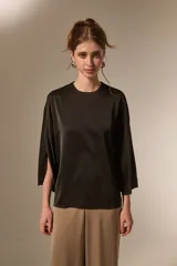 Blusa de satén color negro, con cuello redondo a la base, mangas 3/4 con abertura lateral y diseño holgado.