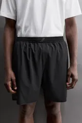 Pantalones cortos negros de tejido técnico perforado, ligeros y elásticos. Cuentan con cintura elástica ajustable con cordón interior, bolsillos frontales, bolsillo trasero de seguridad con cierre de cremallera, perneras con laterales perforados para transpirabilidad, bajo con acabado termofijado y aberturas laterales. Incluye detalle de logo estampado en la pernera.