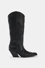 Bota estilo cowboy de caña alta, color negro, con detalles en relieve y costuras decorativas. Presenta punta fina, tiradores laterales y taco cuadrado inclinado.
