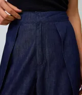 Pantalón wide leg de jean azul oscuro, de talle alto con pretina estructurada, pinzas frontales, sobreposición cruzada y piernas amplias.