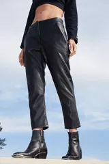 Pantalón sastrero de ecocuero negro, con corte recto, bolsillos delanteros y traseros, y botamanga irregular más corta en la parte frontal.