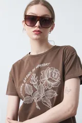 Remera negra de manga corta con estampado botánico en azul y la frase "NOTHING GROWS IN COMFORT".