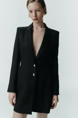 Blazer larga negra con cuello solapa, manga larga y bolsillos de vivo en el delantero. Cierre frontal con dos botones plateados.