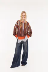 Sweater oversize de corte boxy, color crema con rayas verticales en tonos marrones y detalles de flecos colgantes. Presenta cuello redondo y puños y ruedo en tejido acanalado de color marrón oscuro.