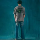 Remera gris de corte oversize con estampa en la espalda de un disco de vinilo sostenido por dos manos.