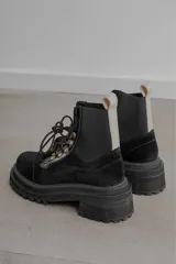 Borcegos de gamuza negra con suela track de goma, cordones frontales y elásticos laterales en color negro con tirador en color beige.