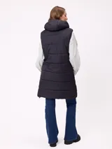 Chaleco largo acolchado color beige, con capucha forrada en sherpa, cierre frontal con cremallera y botones a presión, y bolsillos laterales.