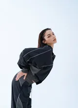 Campera rompeviento negra de estilo deportivo, con cierre frontal completo, cuello alto y detalles de líneas blancas en los hombros y mangas. Presenta puños y cintura elásticos en tono gris oscuro.