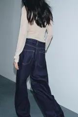 Jeans de tiro alto con pierna ancha, confeccionados en denim azul oscuro. Presentan cinco bolsillos, trabillas en la cintura y un cinturón ajustable del mismo tejido con hebilla metálica. Incluyen pespuntes marcados a tono y cierre frontal con cremallera y botón.