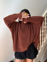 Buzo de punto oversize color rojo, con cuello alto y puños con terminaciones en volados. Presenta detalles en contraste color amarillo en el cuello y los puños, con un tejido de acabado ligeramente brillante.