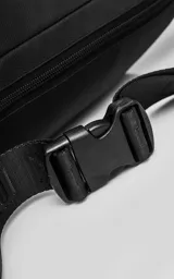 Riñonera negra confeccionada en cordura impermeable de alta resistencia. Presenta tres compartimentos principales con cierres metálicos, un bolsillo lateral adicional y una correa ajustable de alta densidad con broche de seguridad. Incluye una chapa metálica decorativa en el frente.