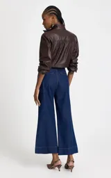 Jean de tiro alto confeccionado en denim azul oscuro, con corte pantacourt de pierna recta y ancha. Presenta cintura estructurada sin pretina, cierre frontal con cremallera y botón, bolsillos traseros y bajo con costuras visibles en contraste.