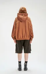 Hoodie oversize color beige con efecto batik, costuras expuestas y recortes estructurales. Presenta capucha amplia y bolsillo frontal tipo canguro.
