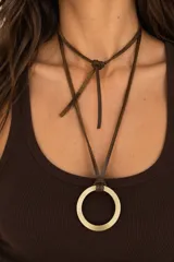 Collar largo de diseño artesanal con cordón de cuero en color chocolate y un dije circular metálico en tono dorado envejecido.