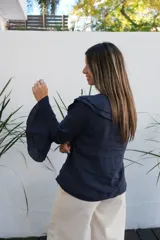 Blusa de lino color azul marino, con cuello con volados, cierre frontal con botones y mangas largas con puños acampanados de doble volado.