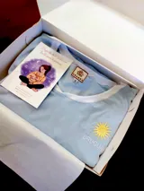 Remera celeste de algodón con cuello redondo y mangas cortas. Tiene un sol bordado en dorado y la palabra "Uruguay" bordada en blanco.