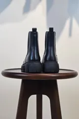Bota tipo Chelsea de caña corta en color beige, confeccionada en material sintético con acabado liso. Presenta paneles elásticos laterales a tono y una suela track robusta y dentada que aporta altura y estilo moderno.