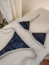 Conjunto de bikini negro con elástico tostado. El corpiño es de corte triangular con breteles regulables y aro metálico en el centro. La bombacha es tipo colaless con tiras laterales regulables.