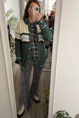 Saco tejido de punto con diseño de ochos, cuello redondo y cierre frontal con botones. Presenta un patrón de rayas horizontales en tonos crema, celeste y bordó sobre una base de color verde oscuro.